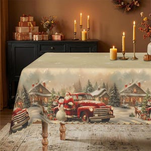 Op de afbeelding: Een rechthoekig tafelkleed met een feestelijke winterscène met een rode vintage truck, de Kerstman, een sneeuwman en besneeuwde huizen. De print bevat dennenbomen en herten tegen een zachte, lichtgekleurde achtergrond met sneeuwvlokken.
