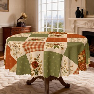 Puede incluir: Un mantel redondo con dise&ntilde;o de patchwork que alterna cuadrados en verde salvia, naranja quemado y crema. El patr&oacute;n incluye motivos florales, peque&ntilde;os puntos blancos y un estampado de cuadros, con un borde festoneado sobre una mesa.