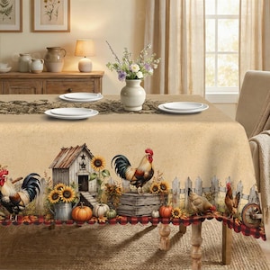 May include: A rectangular tablecloth featuring a beige background with a printed border of roosters, sunflowers, pumpkins, a wooden coop, and a white picket fence. The bottom edge has a red and black buffalo plaid trim. Four white plates are set on top.