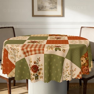 Puede incluir: Un mantel redondo con dise&ntilde;o de patchwork que alterna cuadrados en color crema, verde salvia y naranja quemado. El patr&oacute;n incluye motivos florales, cuadros y delicadas ramas de follaje, con un borde festoneado.