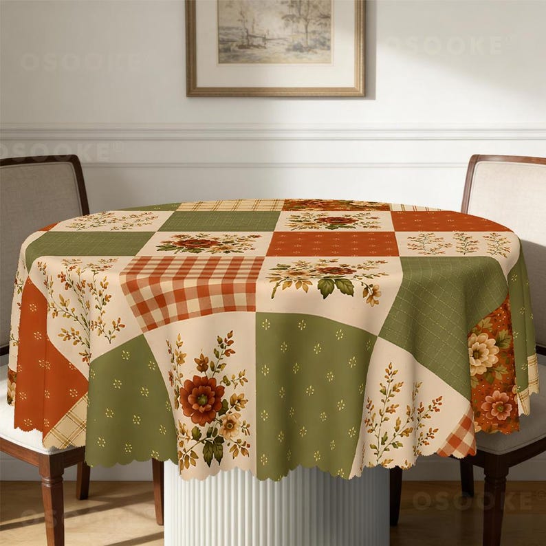 Puede incluir: Un mantel redondo con dise&ntilde;o de patchwork que alterna cuadrados en color crema, verde salvia y naranja quemado. El patr&oacute;n incluye motivos florales, cuadros y delicadas ramas de follaje, con un borde festoneado.