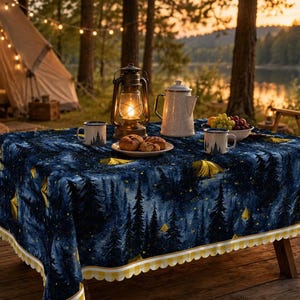 Può includere: Una tovaglia rettangolare con stampa di foresta blu scuro e cielo stellato con accenti di tende gialle. I bordi sono rifiniti con un bordo smerlato a quadretti bianchi e gialli. Il tessuto copre un tavolo con tazze, un piatto e una lanterna.