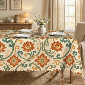 May include: A rectangular tablecloth featuring a repeating pattern of orange lotus flowers and teal swirling vines on a cream background. The fabric drapes over a table set with white plates and a central white vase containing a floral arrangement.