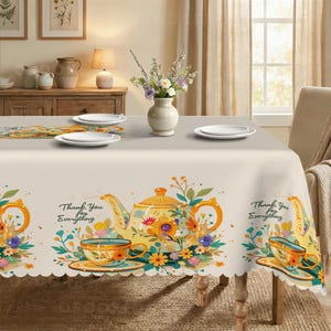 Puede incluir: Un mantel beige con un patrón repetitivo de teteras amarillas, tazas de té naranjas y arreglos florales coloridos. El texto "Thank You for Everything" está impreso en letra negra cerca de cada tetera. Los bordes tienen un diseño festoneado.
