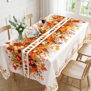 May include: A rectangular white tablecloth featuring a central runner design decorated with autumn motifs including orange pumpkins, red apples, brown pinecones, and colorful fall leaves. The edges have a scalloped trim with gold flourishes.