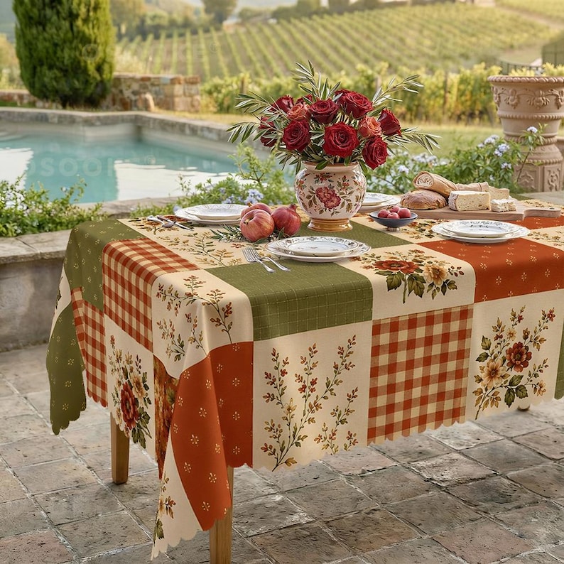 Puede incluir: Un mantel rectangular con un dise&ntilde;o de patchwork de cuadrados en color crema, verde oliva y naranja quemado. El patr&oacute;n incluye motivos florales, ramas de hojas y un estampado de cuadros vichy. Los bordes tienen un acabado festoneado.
