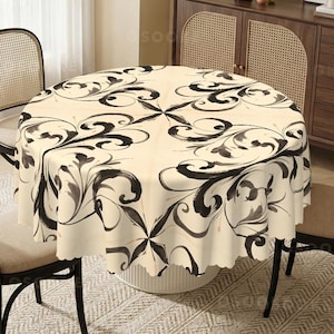 May include: A round tablecloth featuring a cream-colored base with a repeating black and dark gray swirling floral pattern. The fabric has a scalloped edge and drapes over a circular table, displaying a symmetrical design with thin lines.