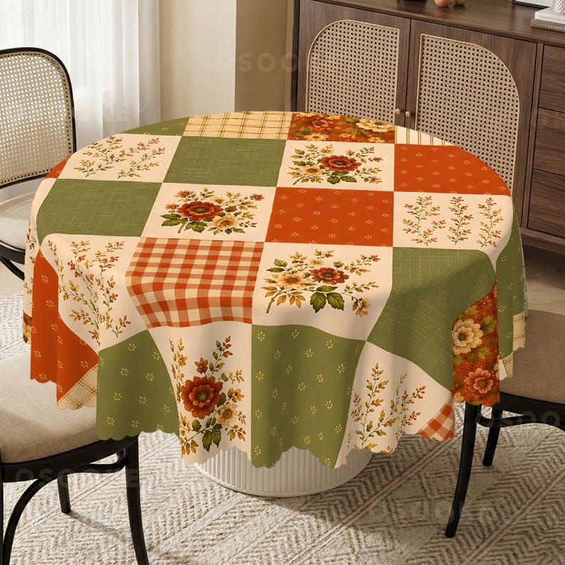 Puede incluir: Un mantel redondo con un dise&ntilde;o de patchwork de cuadrados alternos. El patr&oacute;n incluye tonos verde salvia, crema y naranja quemado con motivos florales, cuadros vichy y peque&ntilde;os puntos. La tela tiene un borde festoneado.