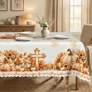 May include: A white tablecloth featuring a repeating autumn-themed pattern of orange and yellow pumpkins, sunflowers, wheat stalks, and crosses. The design includes a scalloped edge and is set with white plates and a central vase of flowers.