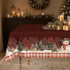 May include: A deep red rectangular tablecloth featuring a winter forest scene with evergreen trees, bare branches, and snowflakes. The design includes a snowman wearing a green hat and red scarf, a fox, and a rabbit, finished with a red and white plaid border.