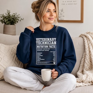 Peut inclure: Sweat-shirt bleu marine avec l'inscription blanche "VETERINARY TECHNICIAN NUTRITION FACTS". Le graphique énumère les valeurs quotidiennes pour la compassion, la patience, le multitâche, le sommeil, la caféine, l'amour des animaux et le dynamisme. Une tasse blanche est tenue.