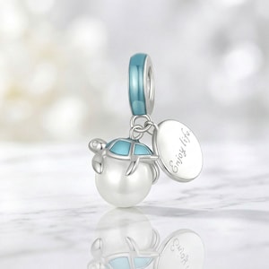 以下が含まれることがあります： 青と白のカメのデザイン、真珠のボディ、小さなダイヤモンドが付いたシルバーチャーム。チャームには青いループと「Enjoy life」と刻まれたシルバーのタグが付いています。チャームはペンダントとして使用するように設計されています。