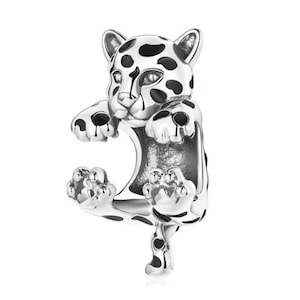 May include: A silver-colored charm in the shape of a leopard cub. The charm has black spots and details, with its paws and ears visible. The leopard is in a playful pose, with its front paws raised.