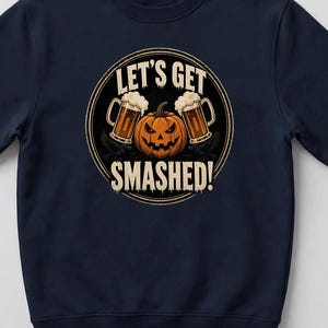 May include: A navy blue crewneck sweatshirt featuring a circular graphic with a central orange jack-o'-lantern flanked by two beer mugs. The text "LET'S GET SMASHED!" is printed in a distressed white font above and below the central imagery.