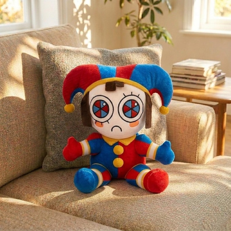 Puede incluir: Mu&ntilde;eco de peluche con disfraz de buf&oacute;n, con una combinaci&oacute;n de colores rojo, azul y amarillo. El mu&ntilde;eco tiene ojos grandes y expresivos y una expresi&oacute;n triste. Est&aacute; sentado en un sof&aacute; beige.