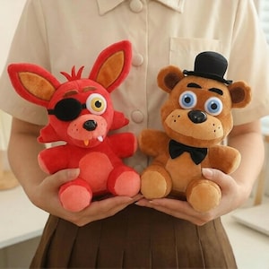 Könnte beinhalten: Zwei Plüschtiere: ein roter Fuchs mit Augenklappe und ein brauner Bär mit schwarzer Fliege und Zylinder. Der Fuchs hat große Ohren und ein gelbes Auge. Der Bär hat blaue Augen und einen freundlichen Ausdruck. Beide sind weich und kuschelig.