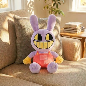 Puede incluir: Un peluche de conejo con una gran sonrisa. El conejo es morado, tiene orejas largas y lleva un mono naranja con guantes amarillos. El juguete est&aacute; sentado en un sof&aacute; beige.