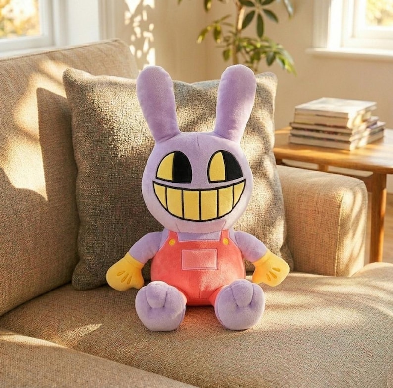 Puede incluir: Un peluche de conejo con una gran sonrisa. El conejo es morado, tiene orejas largas y lleva un mono naranja con guantes amarillos. El juguete est&aacute; sentado en un sof&aacute; beige.