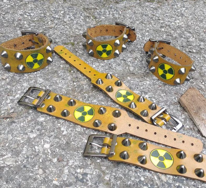 Puede incluir: Cinco pulseras de cuero color amarillo mostaza con tachuelas de metal plateado y un s&iacute;mbolo circular de peligro de radiaci&oacute;n en amarillo y negro. Cada pulsera incluye un cierre de hebilla met&aacute;lica y varios orificios de ajuste.