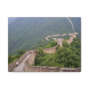 May include: A canvas print of the Great Wall of China. The image shows a section of the wall winding through a lush, green mountain landscape. The wall is made of stone and has a walkway along the top.