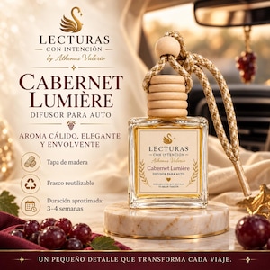 May include: A square glass car diffuser bottle with a light wood cap and a braided gold cord. The label reads Lecturas Con Intención, Cabernet Lumière, and Difusor Para Auto. The bottle sits on a round marble base surrounded by dark red grapes.