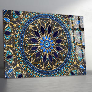 Könnte beinhalten: Dekoratives Panel mit detailliertem Mandala-Design. Das Kunstwerk zeigt ein symmetrisches Muster mit marineblauen, goldenen und hellblauen Punkten und Formen auf dunklem Hintergrund. Das Design erinnert an ein Buntglasfenster.