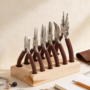 May include: A collection of jewellery-making pliers with brown handles, displayed in a wooden holder. The pliers are of different shapes and sizes, including needle-nose and round-nose. A jewellery-making kit with tools for crafting.