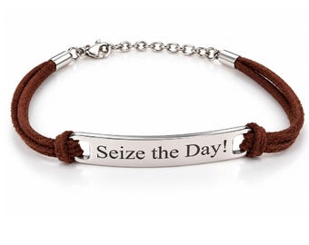 Puede incluir: Una pulsera de cordón marrón con una placa central de metal plateado grabada con el texto Seize the Day!. La pulsera incluye una extensión de cadena plateada y un cierre de mosquetón que une los dos hilos de cordón marrón.