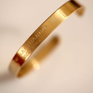 Puede incluir: Pulsera de oro con una bandera americana grabada y el texto "SALABARRIETA 08/16/2014".