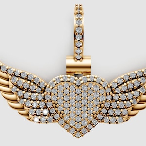 Puede incluir: Colgante dorado con forma de corazón y diseño de alas, adornado con pequeños diamantes. El colgante tiene una anilla para una cadena. Las alas y el corazón están incrustados con pequeñas piedras brillantes.