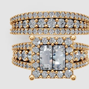 Puede incluir: Juego de anillos de dos piezas en tono dorado con piedras preciosas claras y brillantes. El anillo superior presenta múltiples filas de piedras pequeñas. El anillo inferior tiene una piedra central grande de corte cuadrado, rodeada de piedras más pequeñas.