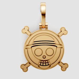 Puede incluir: Colgante dorado con un diseño de calavera y huesos cruzados con un sombrero. El colgante tiene una argolla para sujetarlo a una cadena. La calavera tiene dos ojos circulares y una boca sonriente. Los huesos cruzados están detrás de la calavera.