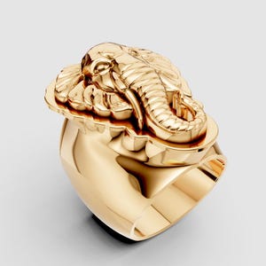 Puede incluir: Un anillo dorado con un diseño de cabeza de elefante. El anillo presenta una cabeza de elefante detallada con una superficie texturizada y una banda lisa y pulida. El anillo está hecho de un metal brillante de color dorado.