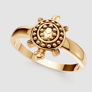 May include: A gold-colored ring featuring a turtle design. The turtle has a detailed shell with small, round accents and a heart-shaped center. The ring's band is smooth and polished, creating a contrast with the textured turtle.