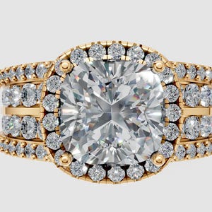 May include: A gold ring with a large, square-cut diamond center stone, surrounded by a halo of smaller diamonds. The band features multiple rows of diamonds, creating a sparkling, luxurious look. The ring is set against a neutral background.