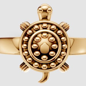 Puede incluir: Un anillo dorado con un diseño de tortuga. El caparazón de la tortuga está detallado con pequeños círculos en relieve, y la cabeza y las patas también son visibles. La banda del anillo es lisa y pulida.