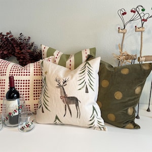 May include: A collection of decorative throw pillows with a Christmas theme. The pillows feature a red and white checked pattern, a green and white tree pattern, a cream pillow with a reindeer and trees, and a green velvet pillow with gold polka dots.