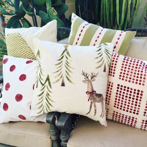May include: Five decorative throw pillows with various festive patterns. The pillows are arranged on a light brown sofa. The patterns include a green and red striped pattern, a green tree pattern with a reindeer, a red polka dot pattern, a red and white polka dot pattern, and a green and white geometric pattern.