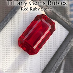 Op de afbeelding: Een helderrode robijn, smaragd geslepen, gepresenteerd in een donkergrijze doos. De tekst "Tiffany Gems Rubies" en "Red Ruby Stone" zijn zichtbaar. De facetten van de robijn reflecteren het licht.