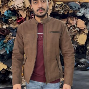 May include: A brown jacket with a mandarin collar, a full-length front zip, and two zipped side pockets. The jacket features a small zipped chest pocket on the left side and a single snap button closure at the neck, worn over a maroon shirt.