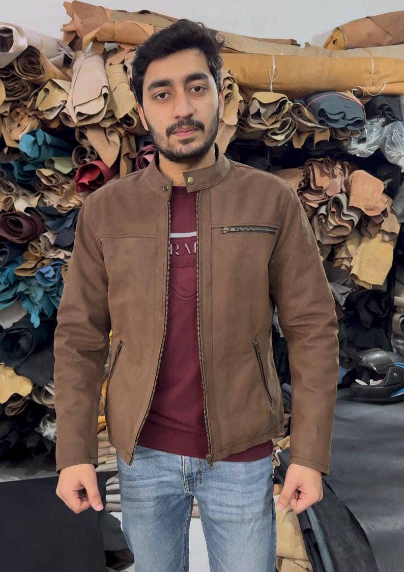 May include: A brown jacket with a mandarin collar, a full-length front zip, and two zipped side pockets. The jacket features a small zipped chest pocket on the left side and a single snap button closure at the neck, worn over a maroon shirt.