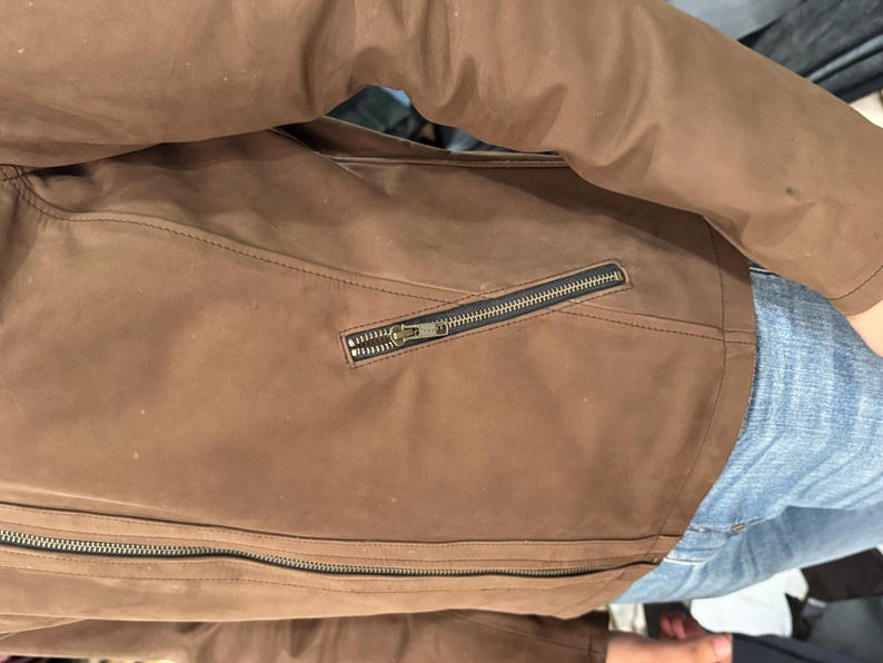 May include: A brown jacket with a smooth, matte finish featuring a long-sleeve design, a full-length front zip, and a diagonal zipped pocket on the side. The garment is constructed with visible seam detailing and dark metal hardware.