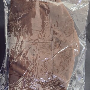 May include: A solid brown garment with visible stitched seams and a rounded neckline, encased in a clear, crinkled plastic protective bag. The fabric appears smooth and matte, with the packaging creating reflective highlights across the surface.