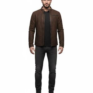 May include: A brown leather jacket with a stand-up collar, a front zip fastening, and a zipped chest pocket. The jacket is worn over a plain black t-shirt, paired with dark grey denim jeans and brown leather boots, creating a complete outfit.