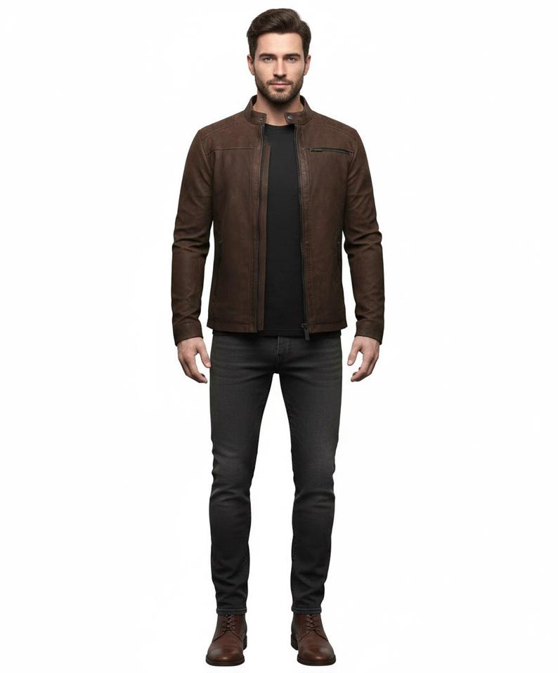 May include: A brown leather jacket with a stand-up collar, a front zip fastening, and a zipped chest pocket. The jacket is worn over a plain black t-shirt, paired with dark grey denim jeans and brown leather boots, creating a complete outfit.
