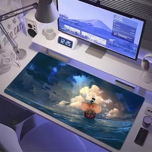 Può includere: Tappetino per mouse rettangolare con una scena nautica di una nave che naviga sull'oceano sotto un cielo nuvoloso. La nave ha un teschio e ossa incrociate sulla sua vela. La tavolozza dei colori include blu, bianchi e arancioni.