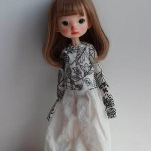 May include: A white ceramic mug with a black handle and the text "But First, Coffee" in a black, handwritten-style font. The mug is on a white surface.