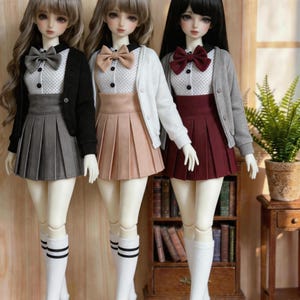 Puede incluir: Tres muñecas de moda vestidas con atuendos inspirados en la escuela. Cada muñeca lleva una falda plisada, una camisa con cuello y pajarita, una rebeca y calcetines hasta la rodilla. Las faldas son grises, melocotón y burdeos.