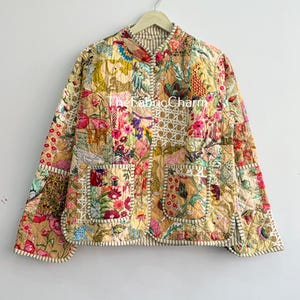 May include: A quilted jacket featuring a patchwork design with various floral and animal patterns in shades of yellow, pink, blue, and green. The jacket has a mandarin collar, long sleeves, two front pockets, and a light-coloured striped trim.