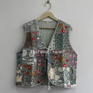 Può includere: Un gilet senza maniche con un design patchwork caratterizzato da motivi floreali grigi, bianchi e rossi. Il capo presenta uno scollo a V, una chiusura frontale a laccio e una fodera interna a righe bianche e nere. Il testo TheFabricCharm è visibile.